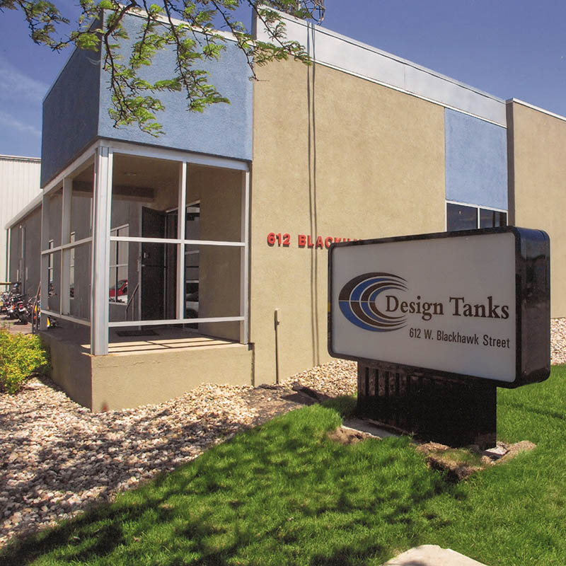 The exterior view of the Design Tanks building located at 612 W. Blackhawn Street in Sioux Falls, SD includes the signage with their logo and an structure with a combination of light blue and tan that blends well with the sky.