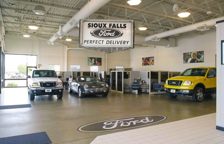 The interior of the Sioux Falls Ford showroom with 3 shiny and new vehicles on 26th street. The exposed industrial ceiling adds a classy and modern feel to the aesthetics.