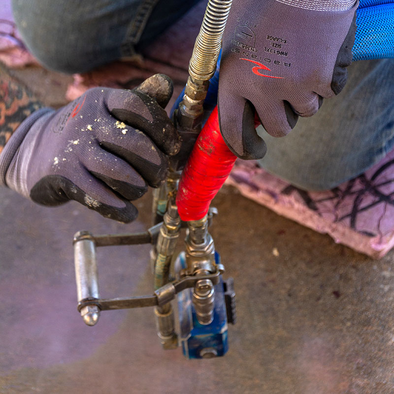 A crew member is kneeling in the job site, wearing grey gloves, and working with a piece of equipment used during the concrete lifting process.