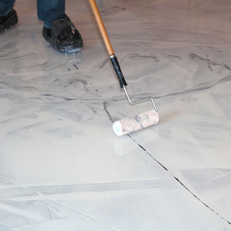 Showing the floor view of a crew member using a rolling brush to apply material to an epoxy floor.